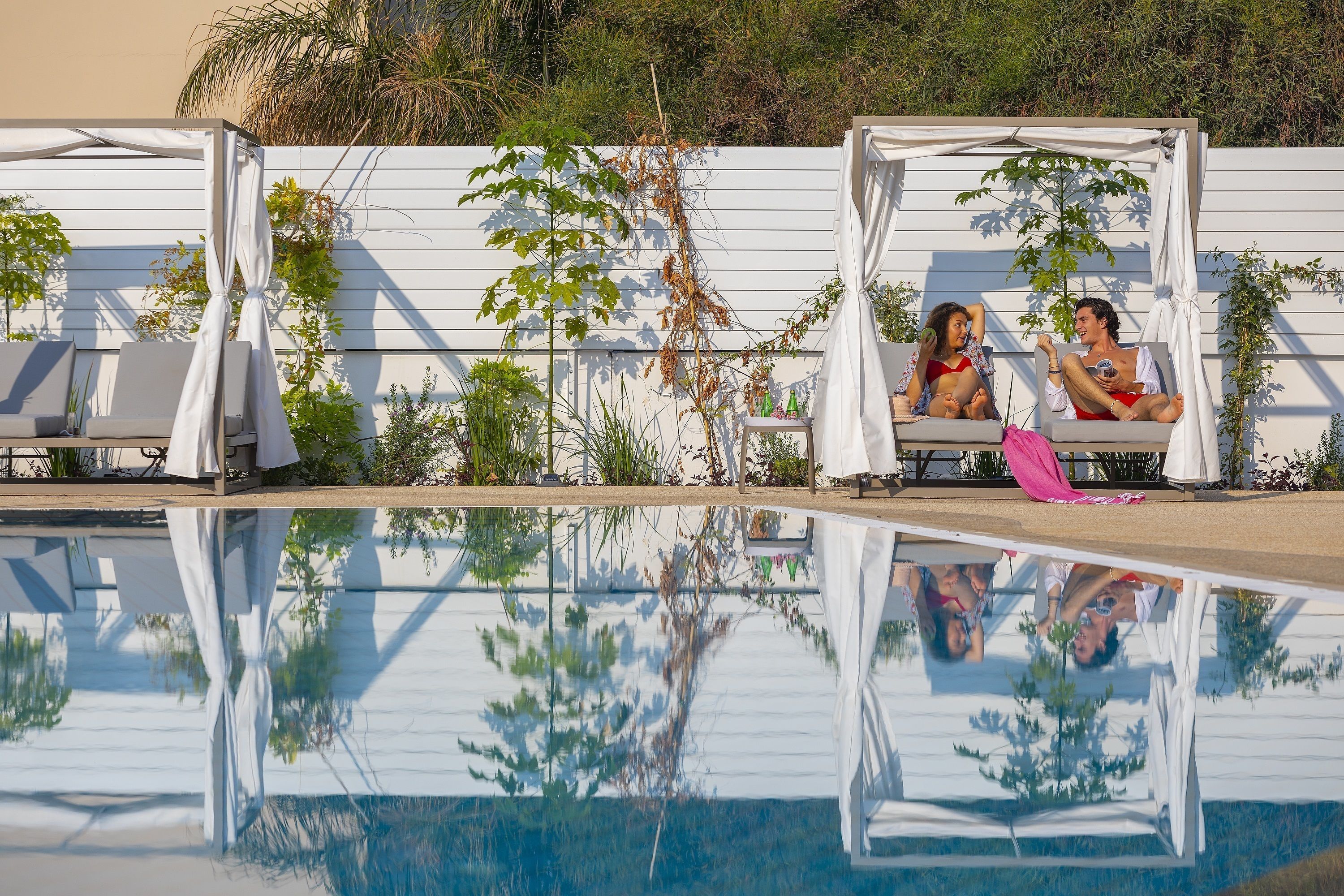 A pool area with two white cabanas, one with a pink towel.