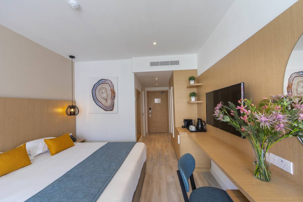 Una habitación de hotel moderna con una cama, un escritorio, una silla, un televisor y un florero con flores.