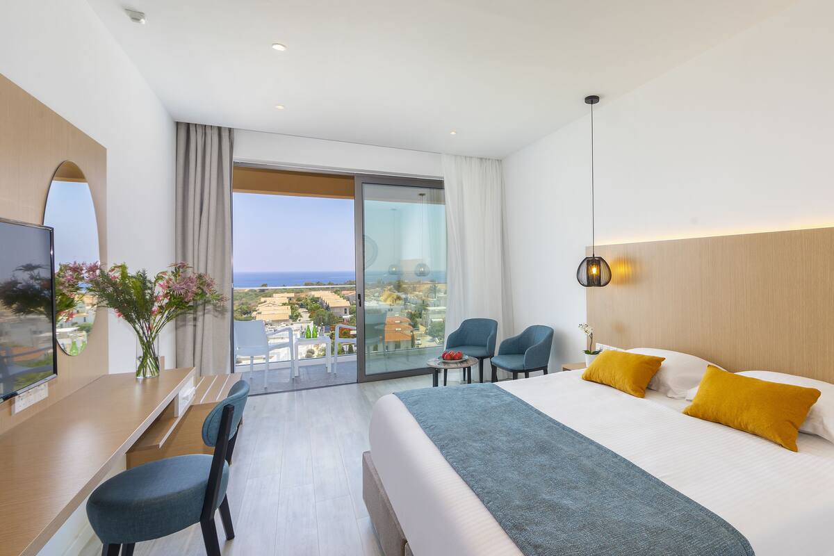 Habitación de hotel con cama, dos sillones, escritorio, televisor y vista a la ciudad.