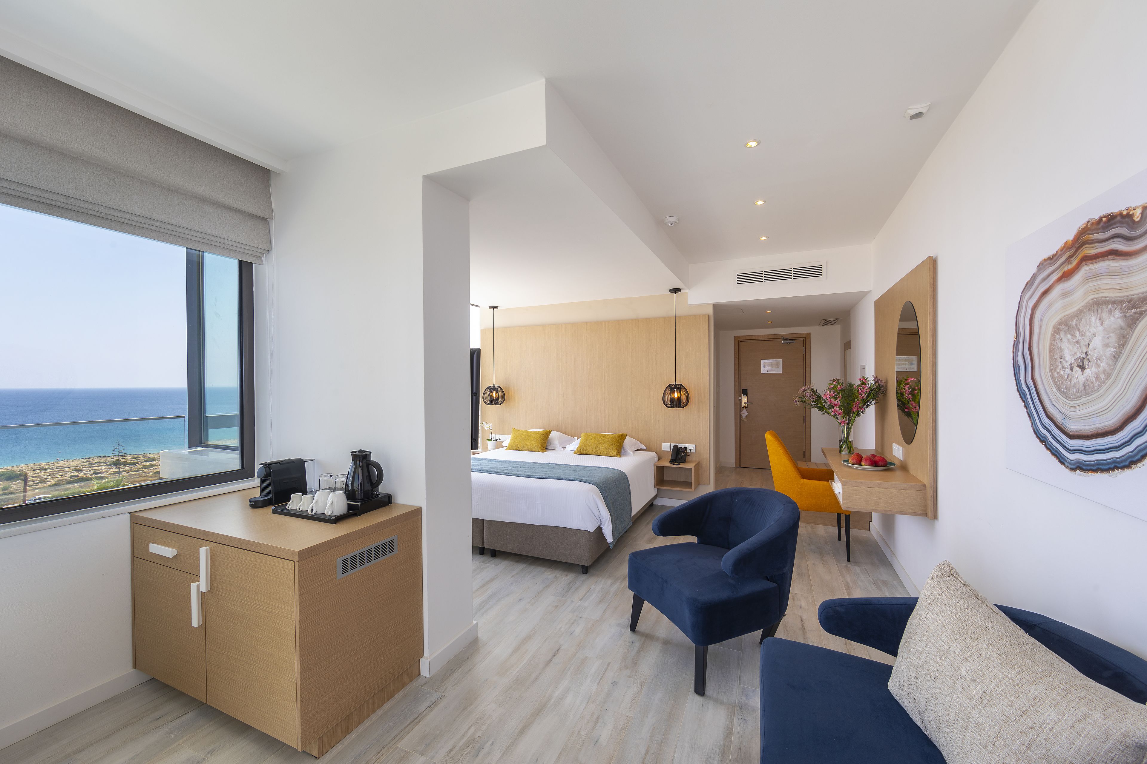 A modern hotel room with a bed, a desk, a chair, and a view of the sea.