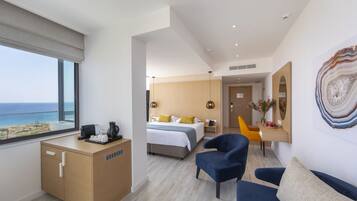 A modern hotel room with a bed, a desk, a chair, and a view of the sea.