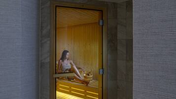 A person sitting in a wooden sauna with a wooden bucket and a wooden bench.