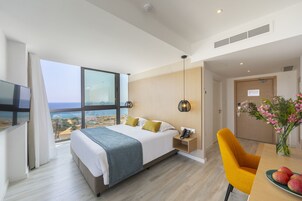Un hotel moderno con una cama grande, un escritorio, una silla, un jarrón con flores y vistas al mar.