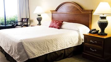 Habitación de hotel con una cama grande, dos lámparas de noche, una mesita con teléfono y una ventana con cortinas.