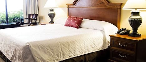 A hotel room with a large bed, two bedside lamps, a nightstand with a phone, and a window with curtains.