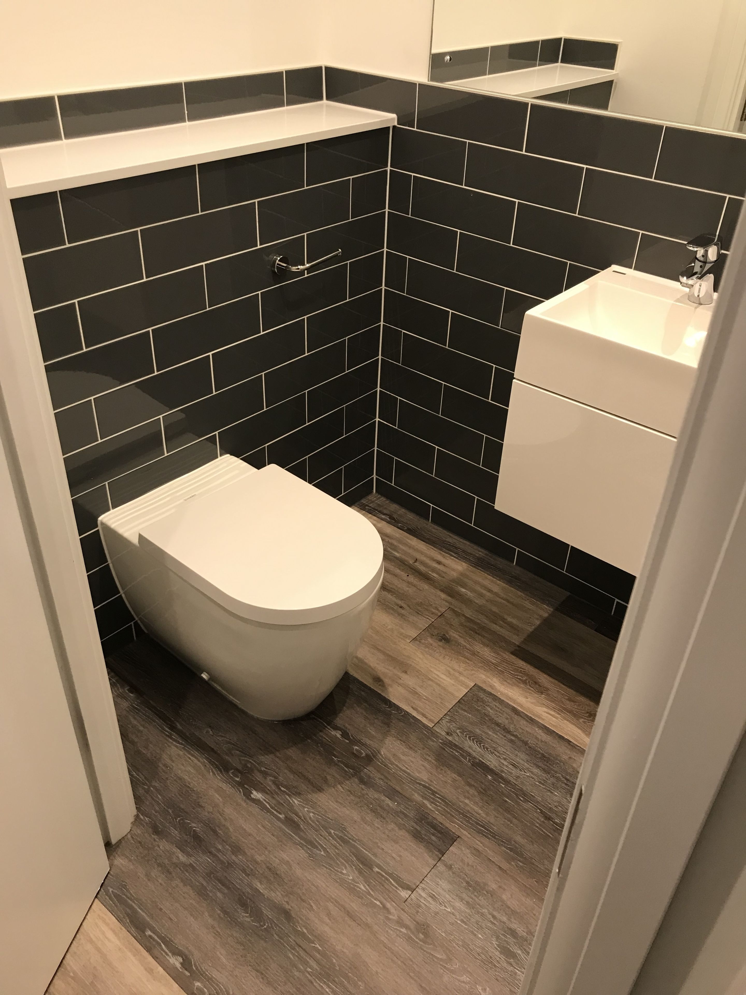 Een kleine badkamer met zwart betegelde wanden, een wit toilet en een witte wastafel.