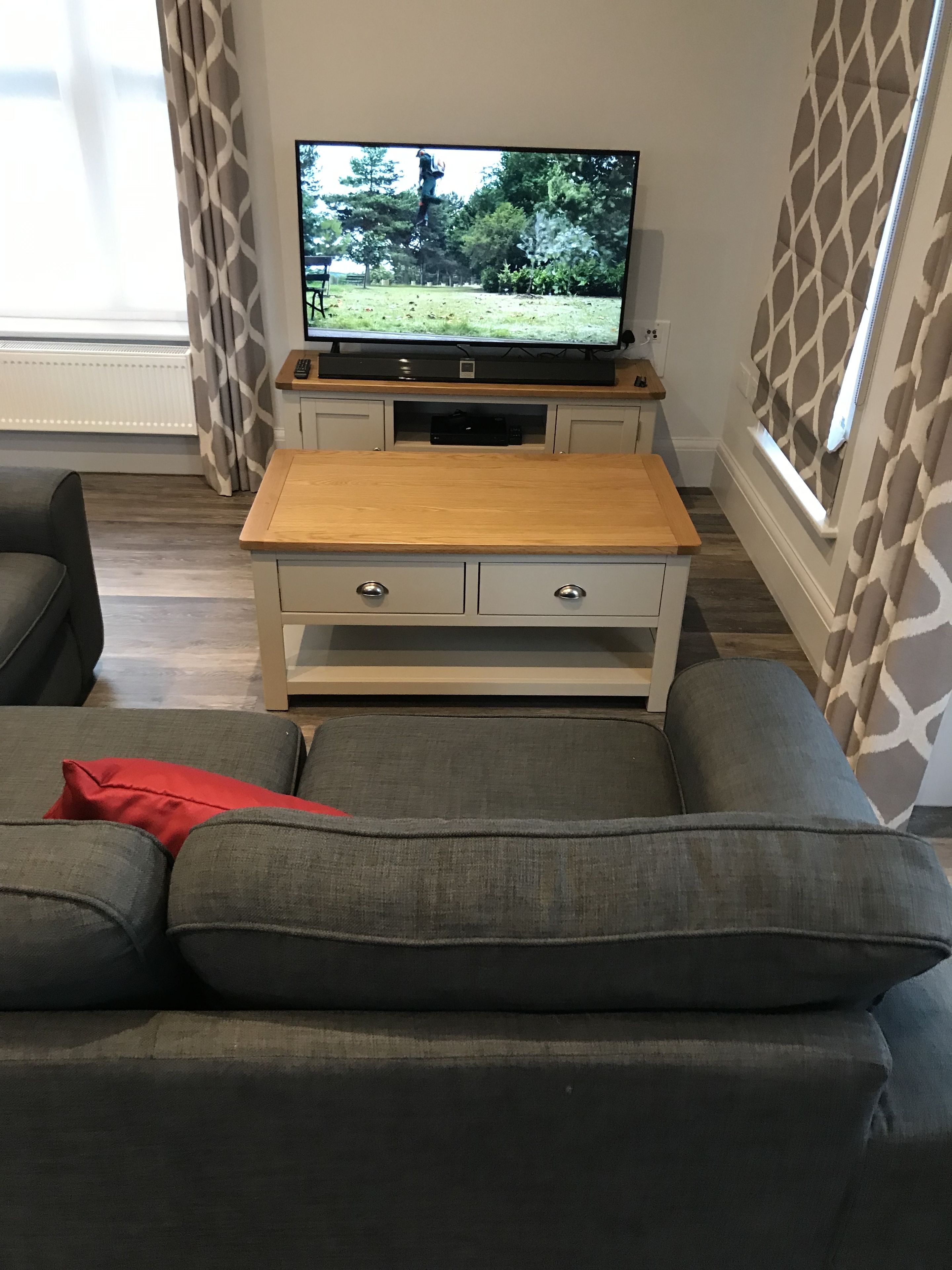 Una sala de estar con un televisor sobre un soporte de madera, sofás grises y cortinas estampadas.