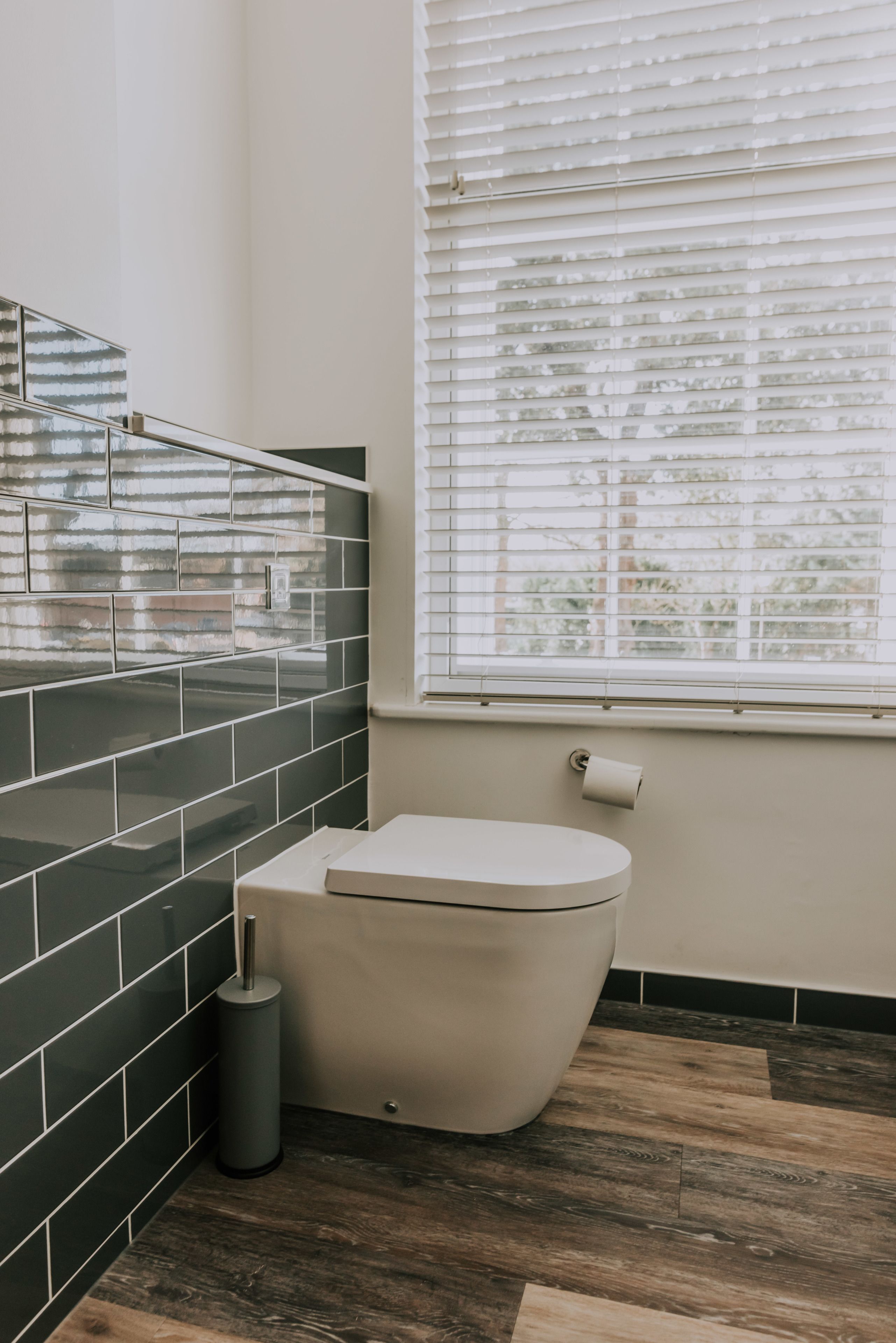 A bathroom with a toilet, a trash can, and a window with blinds.