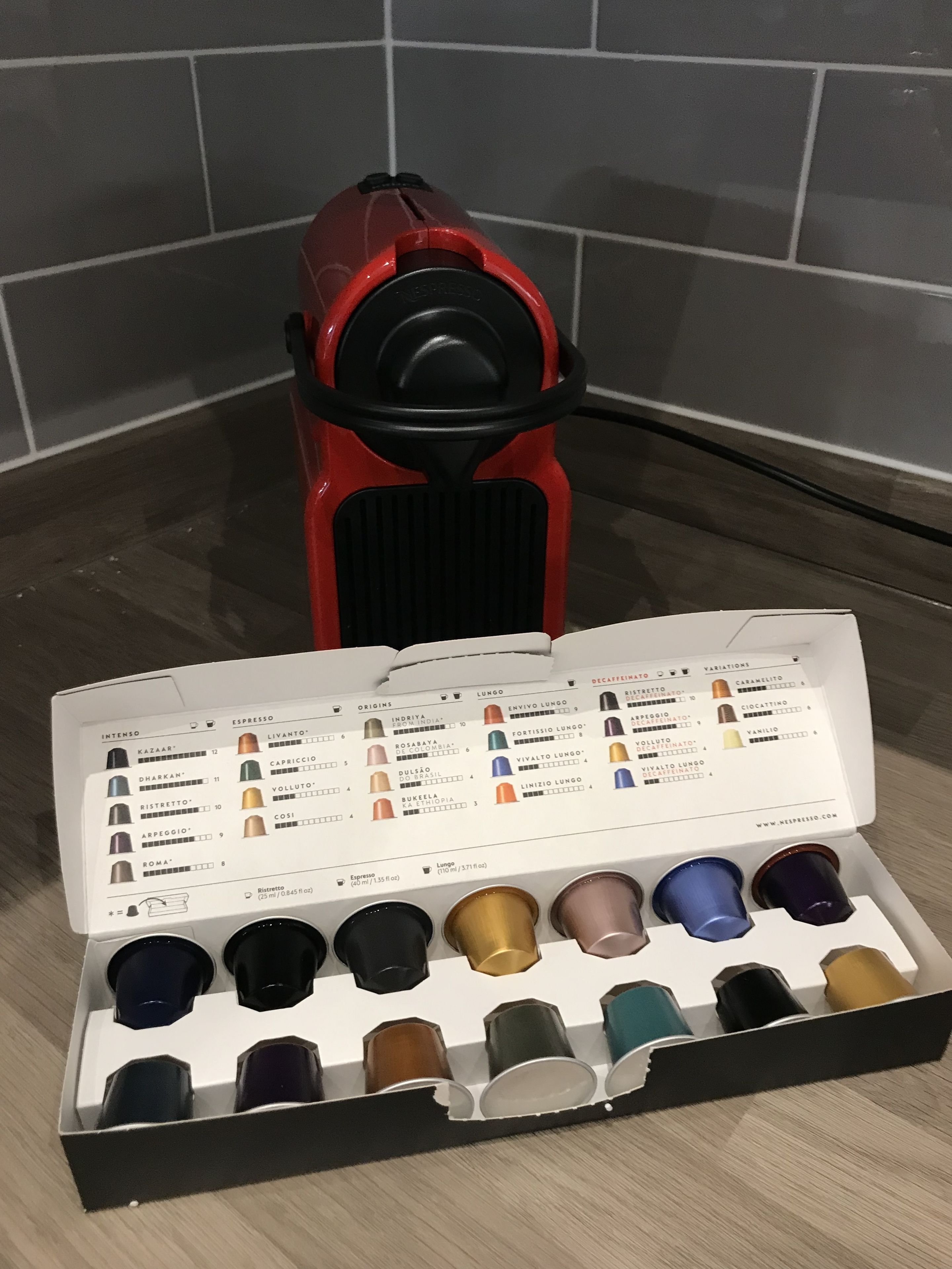 A coffee machine and a box of espresso pods with various flavors.