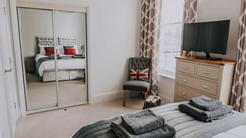 A bedroom with a bed, a chair, a TV, a wardrobe, and a window with curtains.