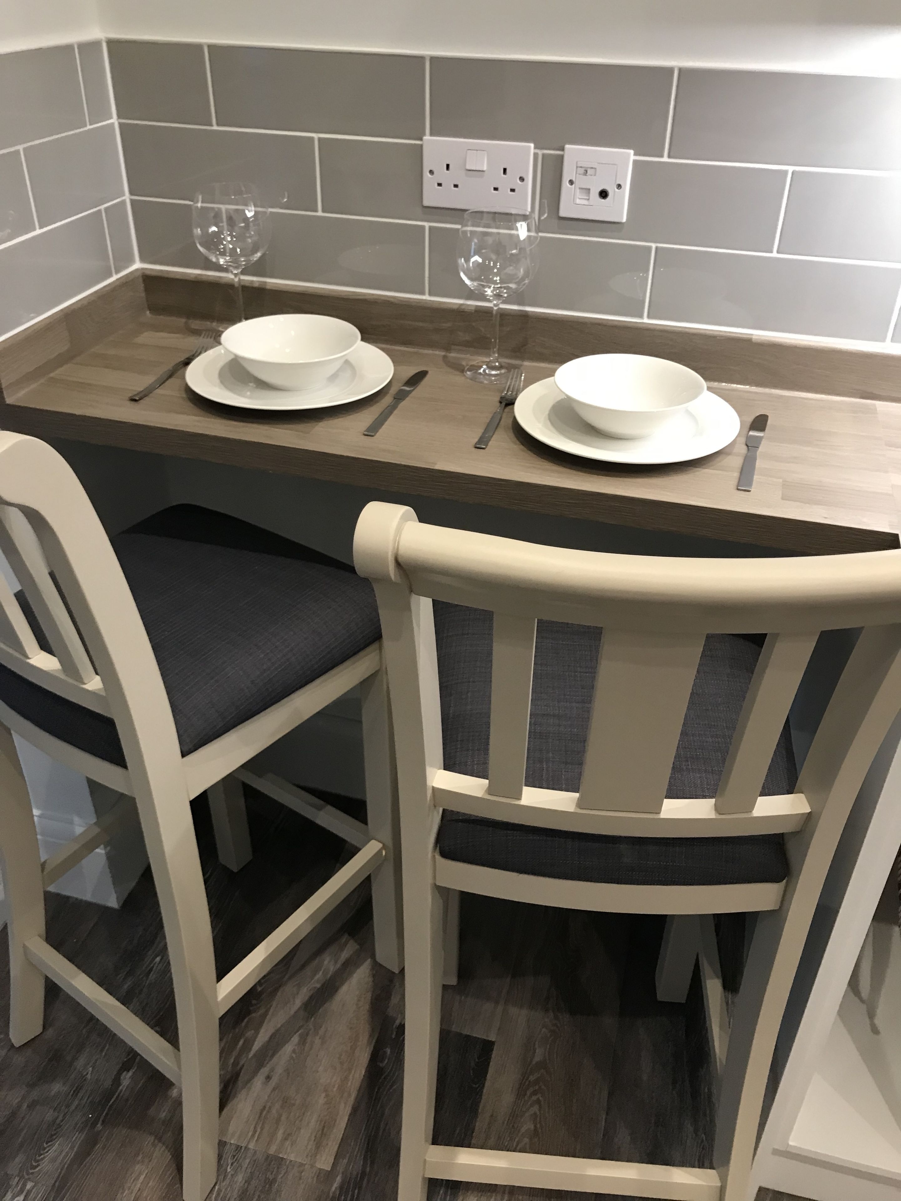 Una mesa de comedor con dos sillas blancas, una copa de vino y un bol a cada lado.