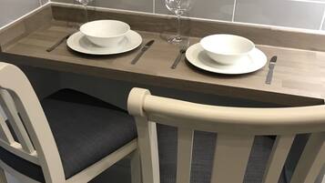 Una mesa de comedor con dos sillas blancas, una copa de vino y un bol a cada lado.