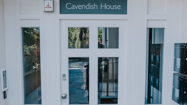 En hvid dør med et skilt, der viser "Cavendish House", og et skilt til brandudgang over den.