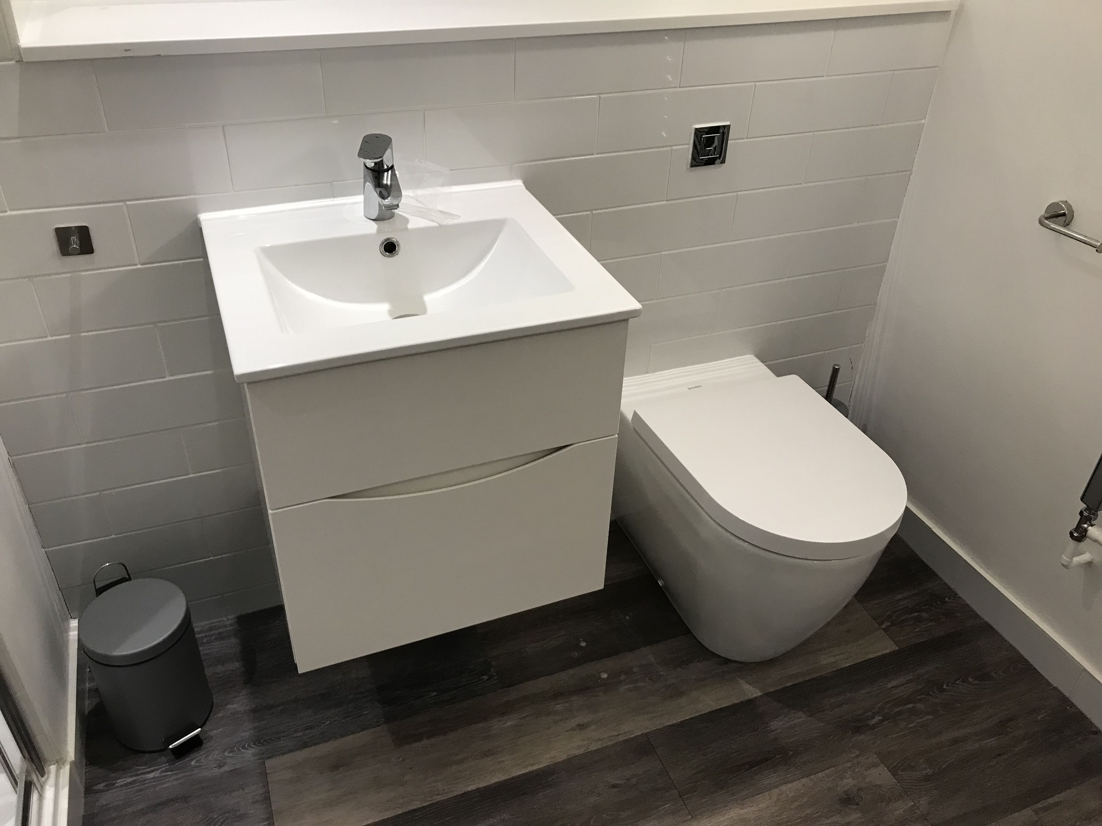 A compact bathroom with a white sink, a toilet, and a trash bin.