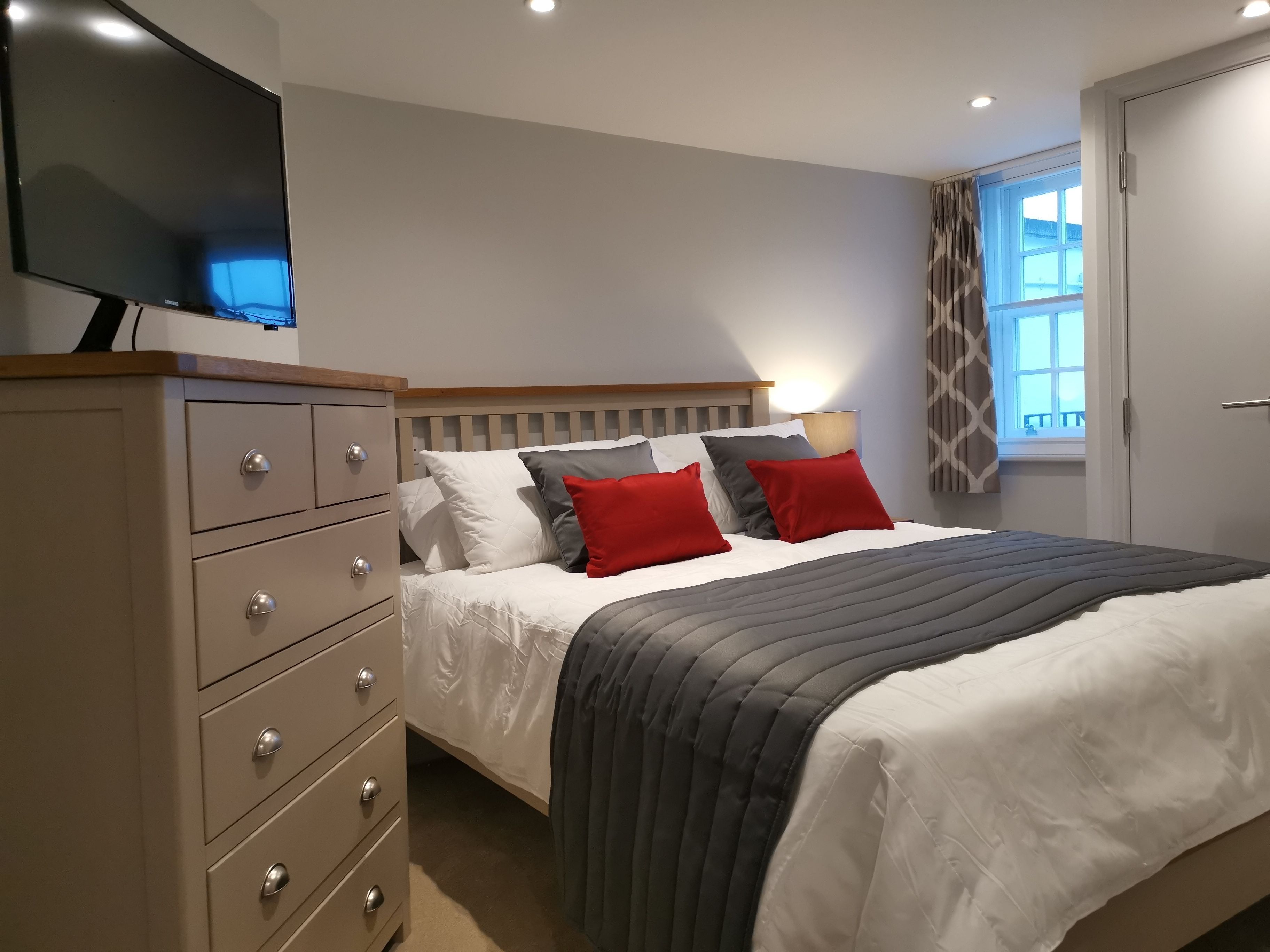 A bedroom with a bed, a dresser, a TV, and a window with curtains.