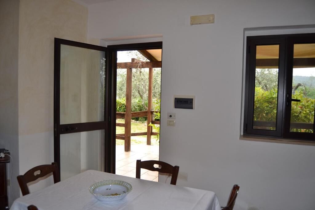 Un comedor con una mesa dispuesta para dos personas, una silla de madera, un tazón de vidrio y una ventana que ofrece vistas a zonas verdes.