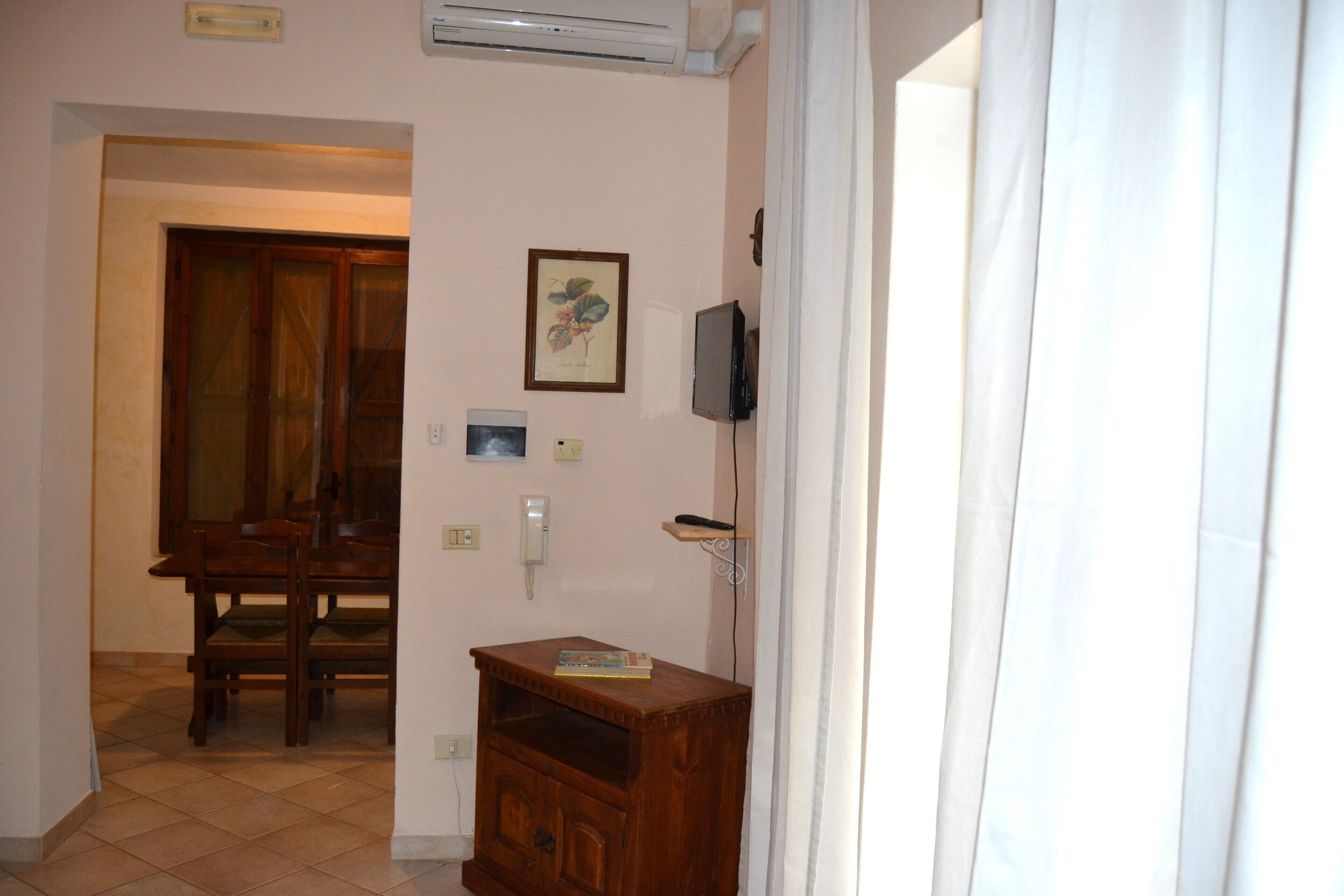 A room with a wooden cabinet, a framed picture on the wall, a television mounted on the wall, and a door leading to another room.