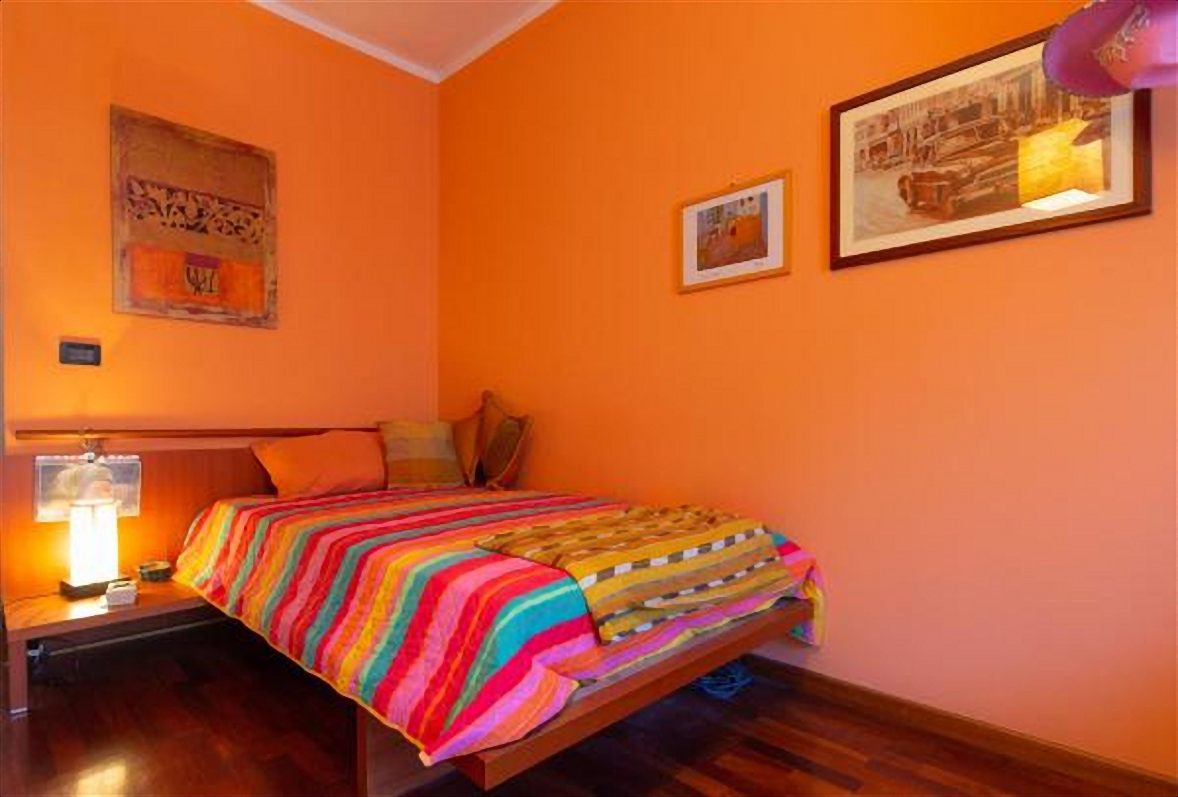 A bedroom with a bed, a nightstand, a lamp, and two framed pictures on the wall.