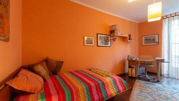 Ein Zimmer mit einem Bett, einem Schreibtisch und einem Sessel. An der Wand hängen drei gerahmte Bilder.