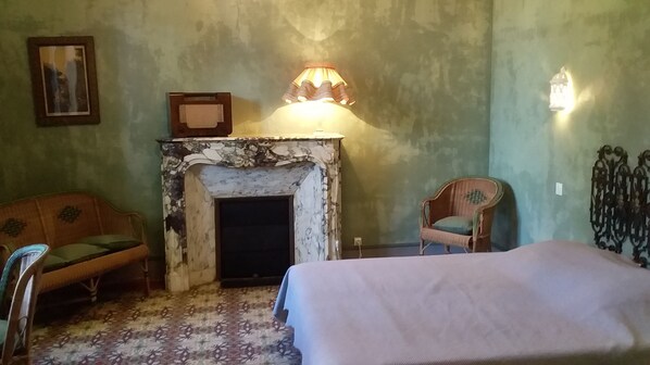 A bedroom with a bed, a chair, a sofa, a fireplace, and a wall-mounted light fixture.