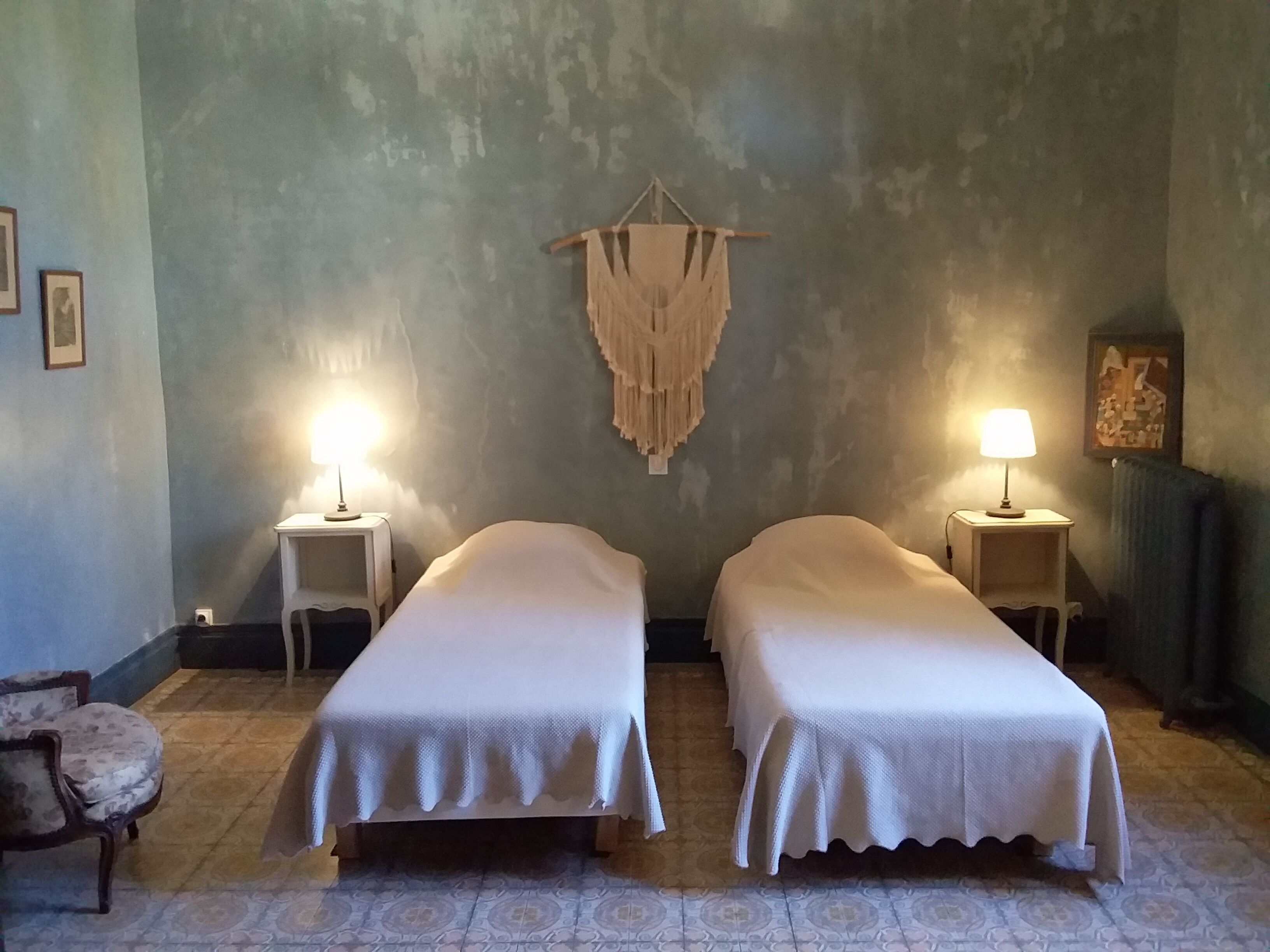 A room with two single beds, a hanging macrame wall decor, and two bedside lamps.