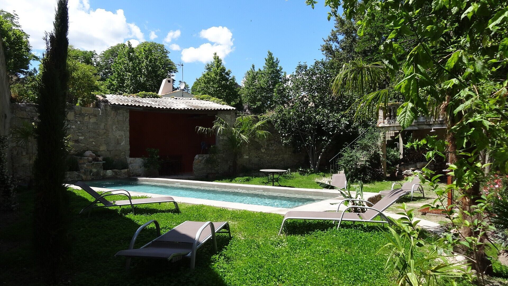 A pool area with lounge chairs, a stone building, and lush greenery.