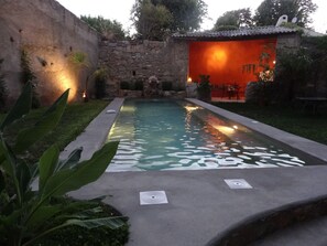 A swimming pool with a stone wall and a small waterfall feature, surrounded by greenery and a patio area with outdoor seating. - House of CHARACTER with SWIMMING POOL in an AUTHENTIC VILLAGE, NEAR the SEA (Capestang)