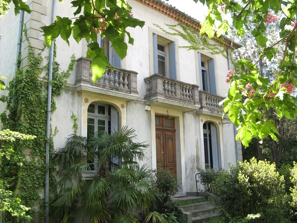 A two-story building with a balcony, a wooden door, and a staircase leading to the entrance. - House of CHARACTER with SWIMMING POOL in an AUTHENTIC VILLAGE, NEAR the SEA (Capestang)