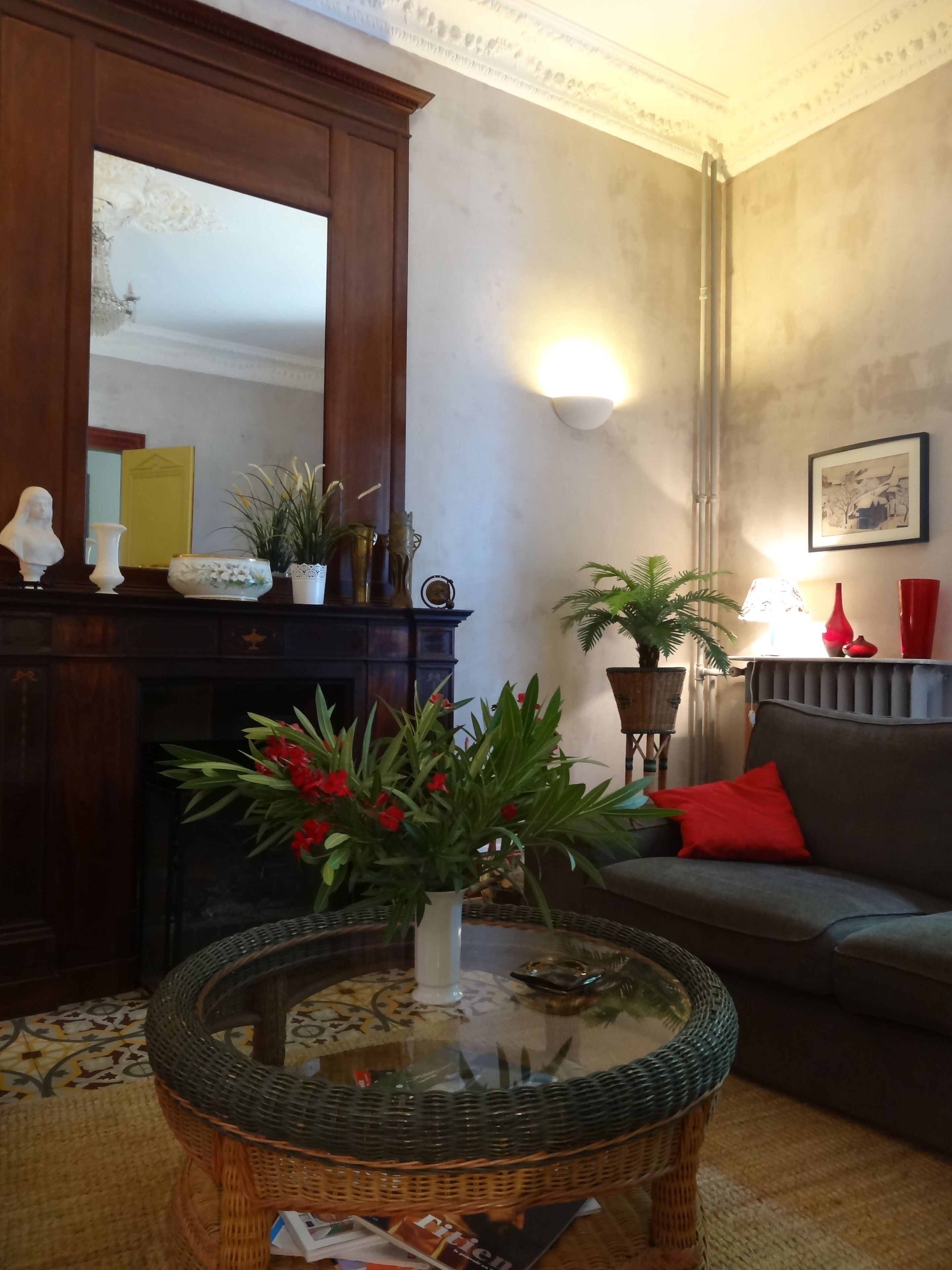 A living room with a fireplace, a sofa, a coffee table with a vase of flowers, and a wall-mounted lamp.