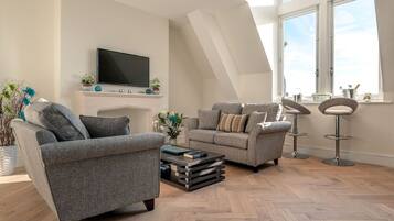 A modern living room with two grey sofas, a flat-screen TV, a fireplace, and a large window with a view.