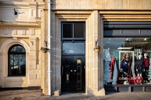 A building facade with a black door, a window with a tree reflection, and a storefront with mannequins and a Christmas tree. - Cathedral View (Exeter)