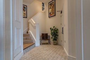 A hallway with a staircase, a chair, and a potted plant. - Cathedral View (Exeter)
