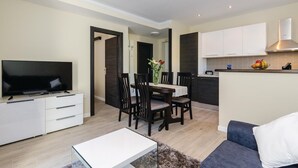 A modern living room with a flat-screen TV, a dining table with chairs, a sofa, and a kitchen area with cabinets and a countertop. - 1 bedroom cozy home in Gruda (Gruda)