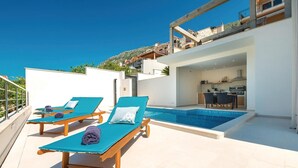 Un espace piscine aménagé sur le toit, avec des chaises longues et une cuisine visible à travers une porte ouverte.