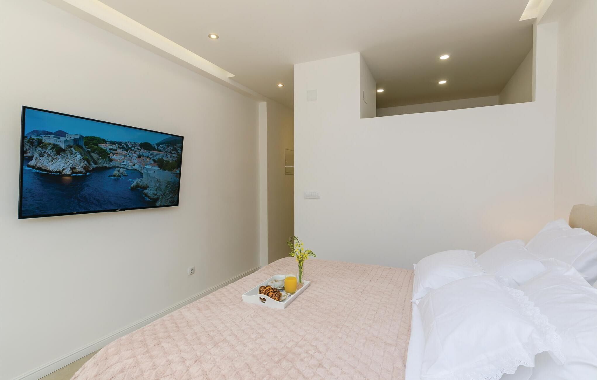 A bedroom with a bed, a bedside table with a tray of breakfast, a painting of a coastal scene, and a small window.