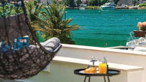 Un balcon donnant sur une mer turquoise, un fauteuil suspendu et une petite table avec une boisson et une pâtisserie.