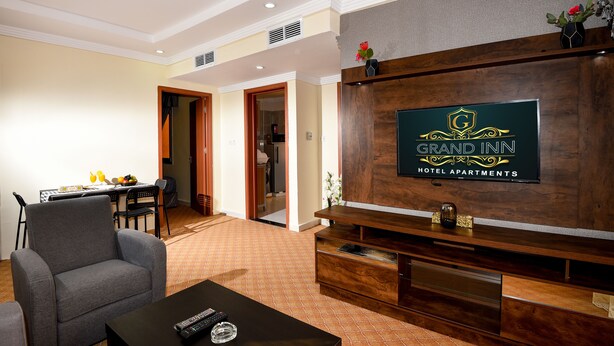 Un salón de hotel con televisor, un sofá, una mesa de centro y una zona de comedor con una mesa y sillas.