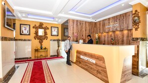 Zona de recepción de un hotel Grand Inn con un mostrador de madera, cuadros enmarcados y una alfombra roja.