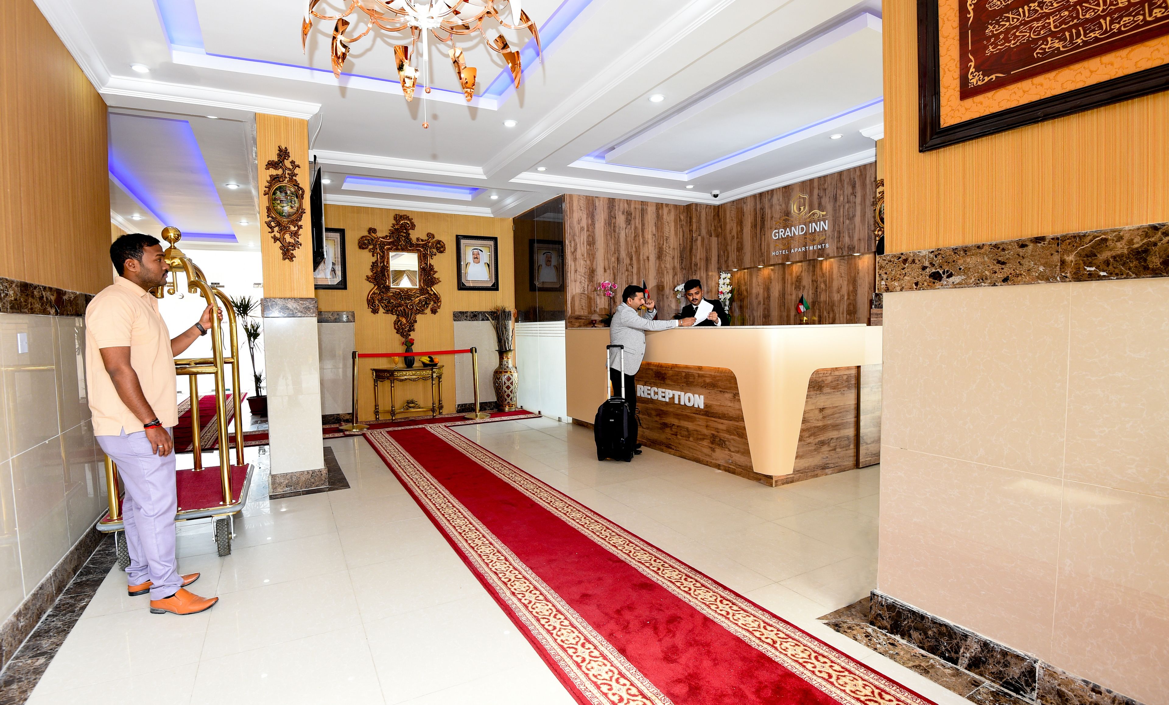 Zona de recepción de un hotel con alfombra roja, mostrador de recepción y candelabro.
