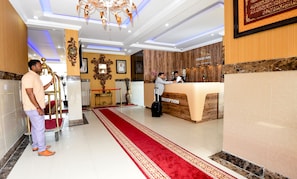 A hotel reception area with a red carpet, a reception desk, and a chandelier.