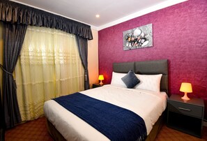 A hotel room with a bed, two bedside tables with lamps, a large window with curtains, and a wall painting.