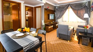Habitación de hotel con comedor, sofá, televisor y ventana con cortinas.