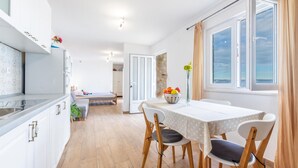 A modern kitchen with white cabinets, a dining area with a table and chairs, and a view of the sea through large windows. - Beach front studio in Poljica with WiFi (Poljica)