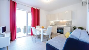 Un apartamento moderno con comedor, kitchenette y balcón con cortinas rojas.