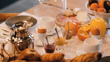 Mesa de café da manhã com croissants, ovos, suco de laranja e uma cafeteira.