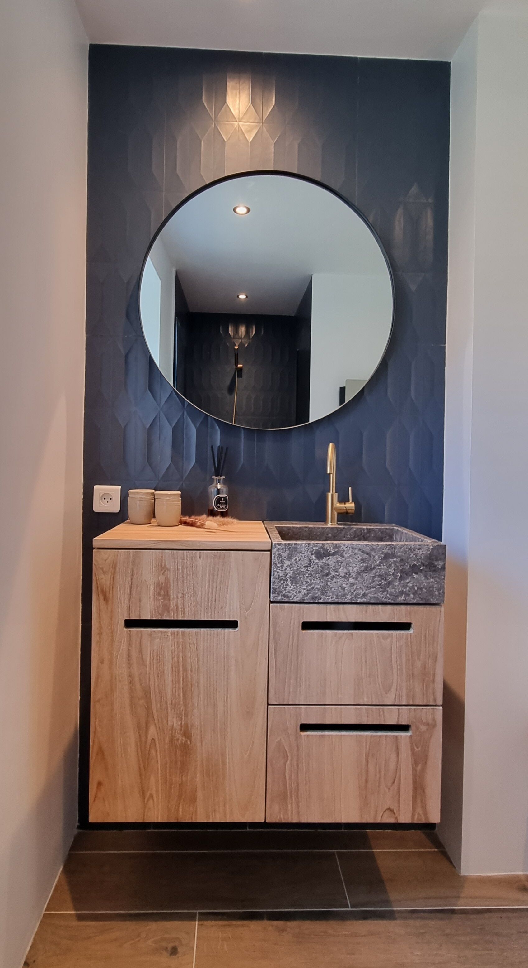 A modern bathroom with a wooden vanity, a round mirror, and a geometric wall design.