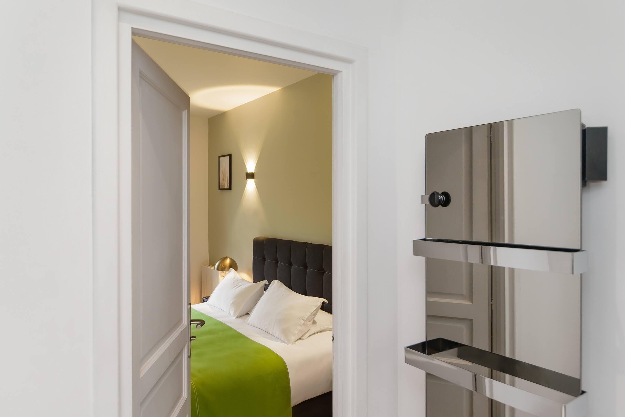 A hotel room with a bed, a bedside table, a wall-mounted TV, and a door.