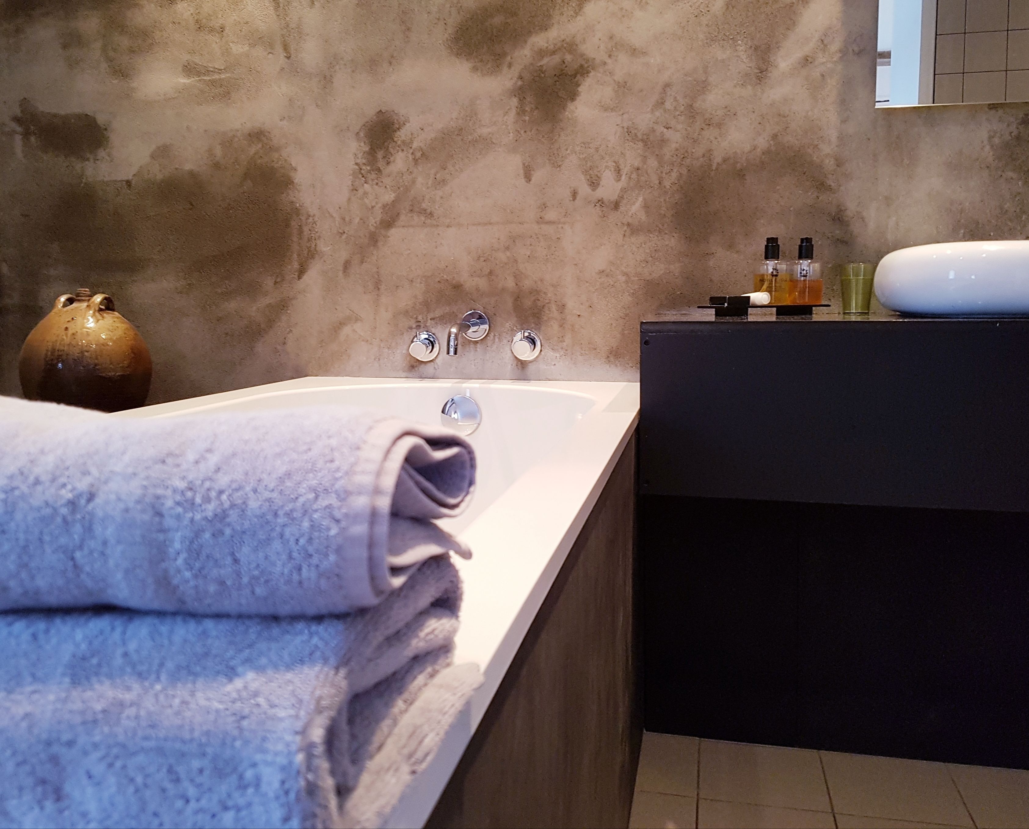 A modern bathroom with a large bathtub, a dark wooden vanity, and a beige textured wall.