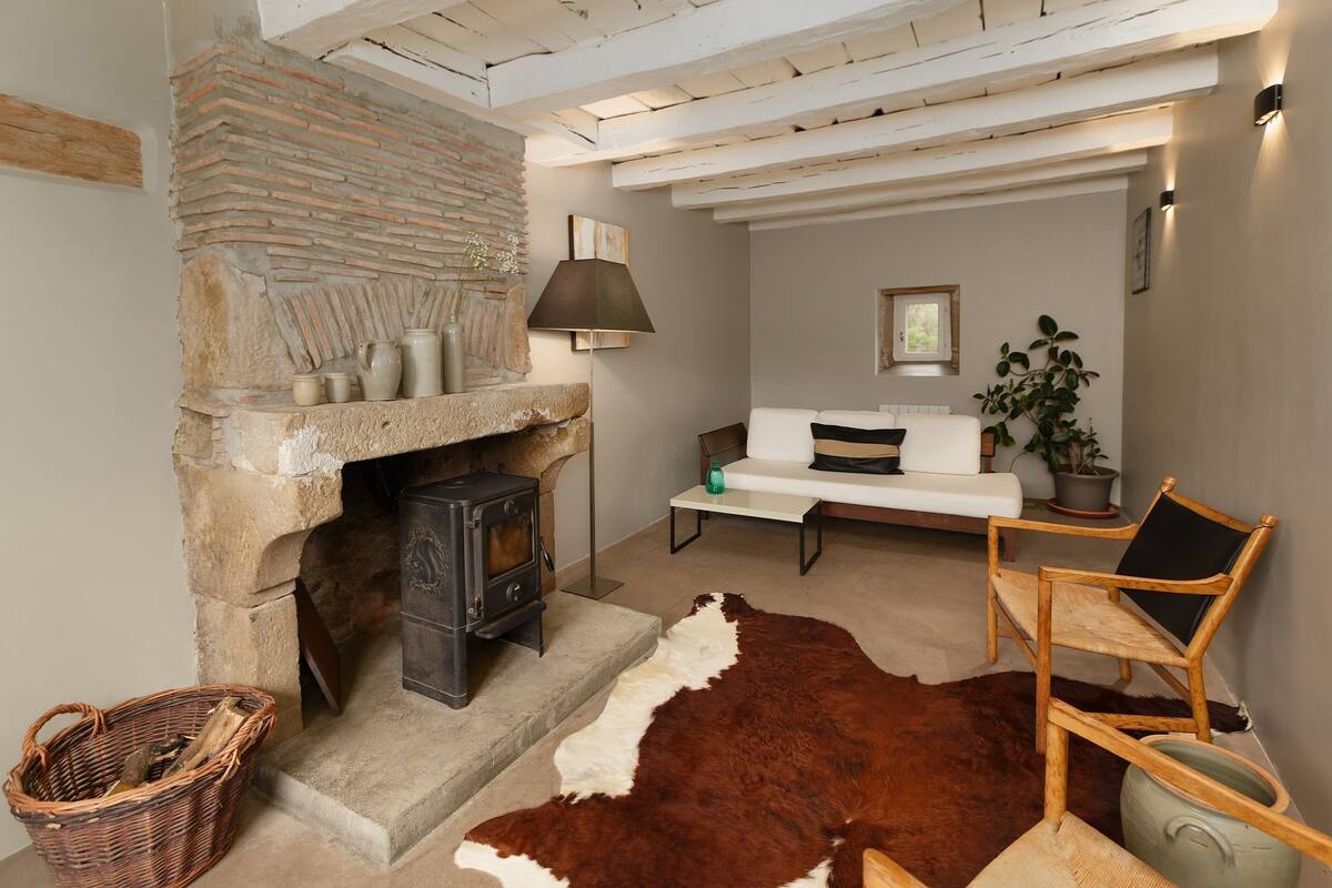 Una sala de estar acogedora con chimenea de piedra, un sofá blanco, un sillón de madera y un tapiz de cuero de vaca.