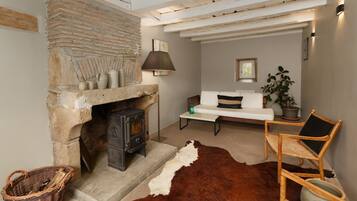 A cozy living room with a stone fireplace, a white sofa, a wooden chair, and a cowhide rug.